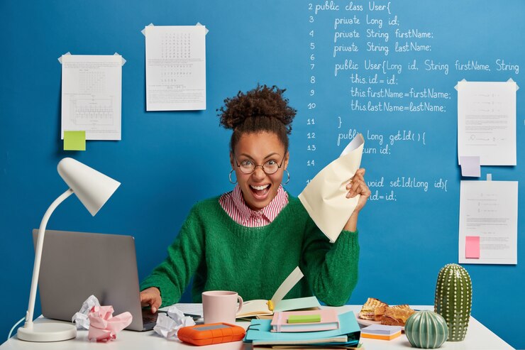 Photo gratuit rédacteur féminin à la peau sombre émotionnelle froisse les papiers dans la main, fonctionne sur un ordinateur portable moderne, écrit des informations dans le bloc-notes