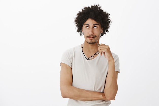 Photo gratuite réfléchi bel homme tenant des lunettes et rêvasser, à la recherche dans le coin supérieur gauche et penser