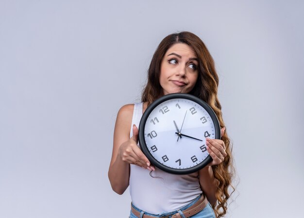 Réfléchi jeune belle fille tenant horloge regardant côté droit sur un mur blanc isolé avec copie espace