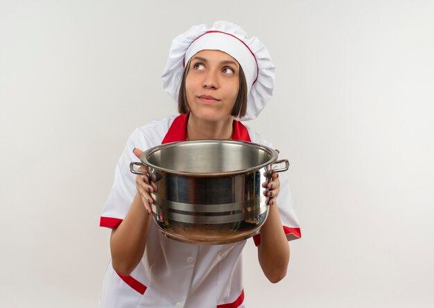 Photo gratuite réfléchi jeune femme cuisinier en uniforme de chef holding pot et levant isolé sur mur blanc