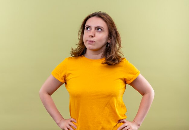 Réfléchi jeune femme décontractée avec les mains sur la taille sur un mur vert isolé