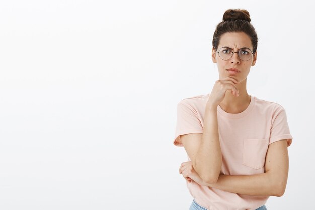 Réfléchi jeune femme élégante posant contre le mur blanc