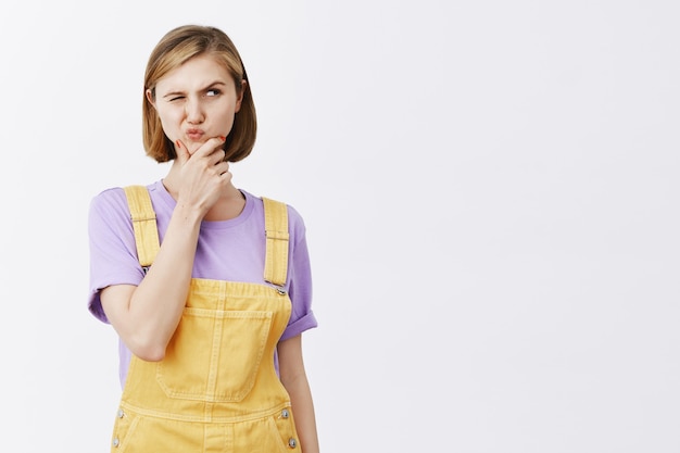 Photo gratuite réfléchi jeune femme méfiante fronçant les sourcils et à droite curieux, penser, prendre une décision