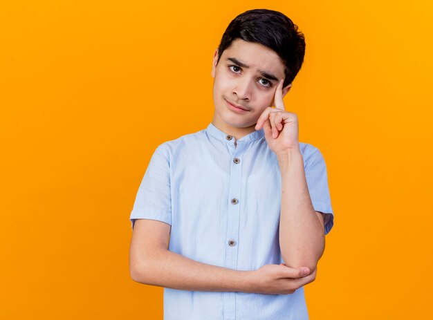 Réfléchi jeune garçon caucasien regardant la caméra faisant penser geste isolé sur fond orange avec copie espace