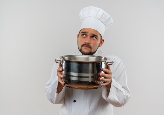 Réfléchi jeune homme cuisinier en uniforme de chef tenant le pot et levant isolé sur un espace blanc