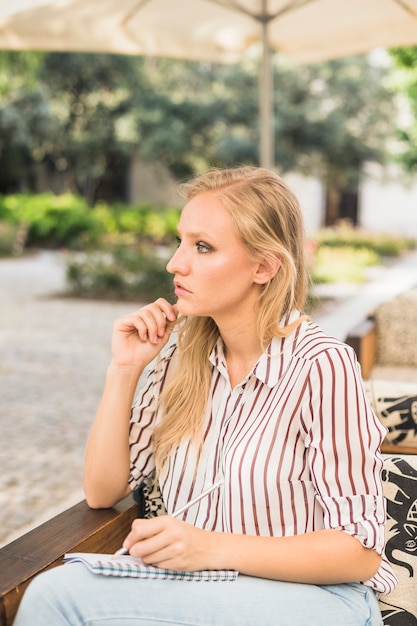 Réfléchie belle jeune femme écrivant sur ordinateur portable avec un crayon