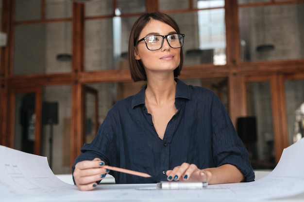 Réfléchie femme d'affaires souriant à lunettes assis près de la table
