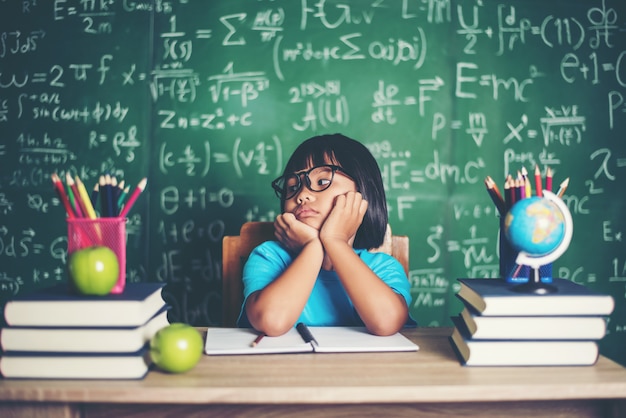 Réfléchie petite fille avec un livre près d&#39;une commission scolaire