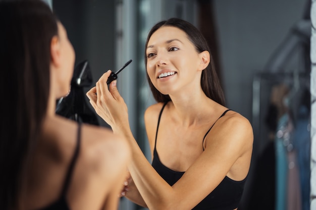 Reflet de la belle jeune femme appliquant son maquillage, regardant dans un miroir