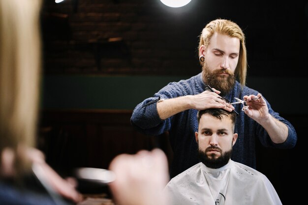 Réflexion du barbier coupant les cheveux de l&#39;homme devant le miroir