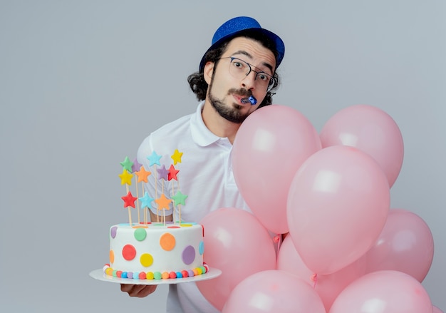 Photo gratuite regardant la caméra bel homme portant des lunettes et un chapeau bleu tenant un gâteau avec des ballons et un coup de sifflet isolé sur fond blanc