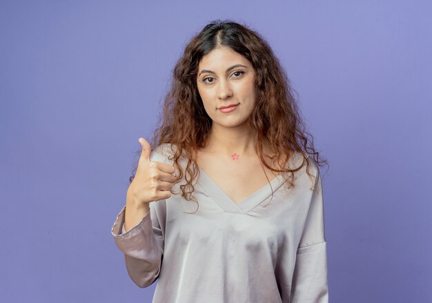 Regardant la caméra jeune jolie fille son pouce vers le haut isolé sur fond bleu