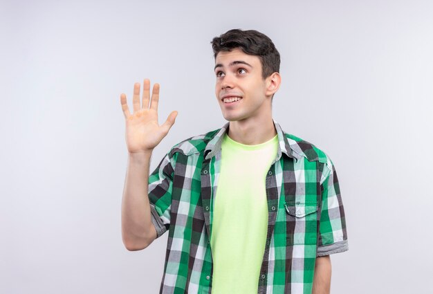 Regardant le côté caucasien jeune homme portant une chemise verte donnant saluer sur mur blanc isolé