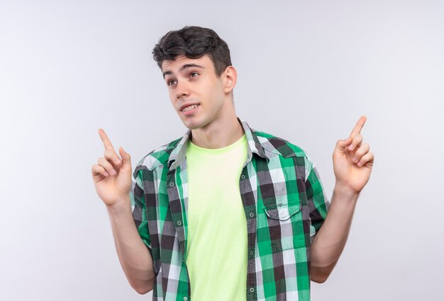 Regardant le côté caucasien jeune homme portant une chemise verte pointe vers le haut sur un mur blanc isolé