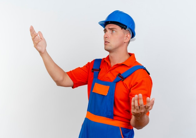 Regardant à côté confus jeune constructeur de sexe masculin portant l'uniforme et un casque de sécurité faisant semblant de tenir quelque chose