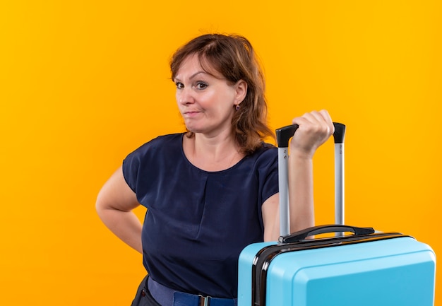 Regardant à côté femme voyageur d'âge moyen tenant valise sur mur jaune isolé