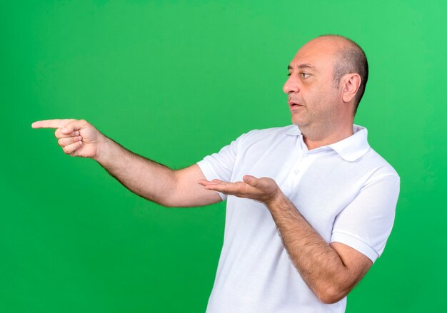 Regardant à côté l'homme mûr occasionnel points à côté isolé sur mur vert