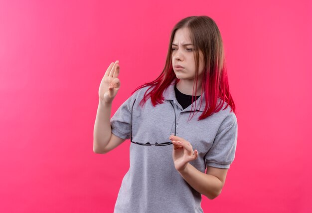 Photo gratuite regardant à côté jeune belle fille portant un t-shirt gris tenant des lunettes montrant le geste okey sur fond rose isolé avec espace de copie