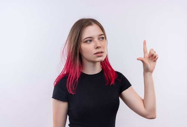 Regardant le côté jeune belle fille portant un t-shirt noir pointe le doigt vers le haut sur fond blanc isolé