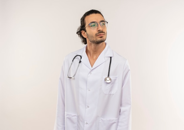 Regardant à côté jeune médecin de sexe masculin avec des lunettes optiques portant une robe blanche avec stéthoscope