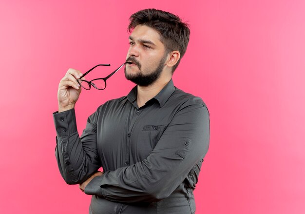 Regardant le côté pensant jeune homme d'affaires touchant la bouche avec des lunettes isolé sur un mur rose