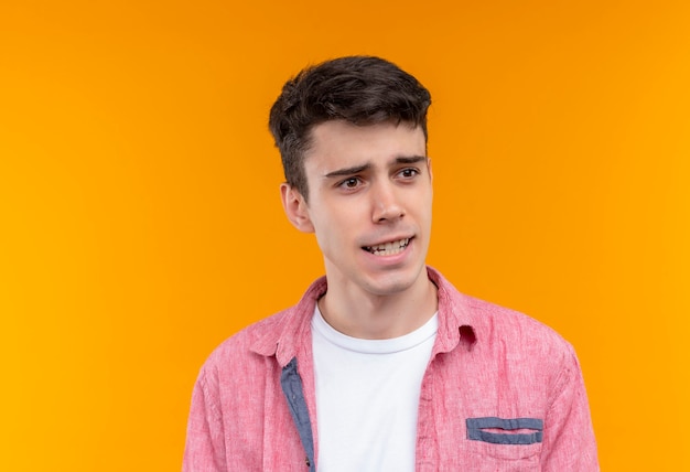 Regardant à côté de la pensée caucasien jeune homme portant une chemise rose sur un mur orange isolé