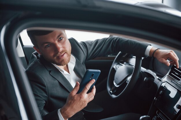 Regardant par la fenêtre. Homme d'affaires moderne essayant sa nouvelle voiture dans le salon automobile