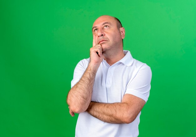 Regardant la pensée de l'homme mûr occasionnel mettant la main sur la joue isolé sur le mur vert