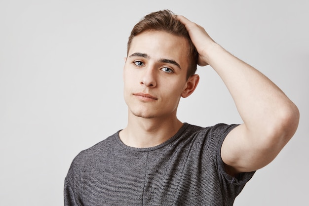 Regardant sérieusement jeune bel homme aux yeux bleus touchant ses cheveux.