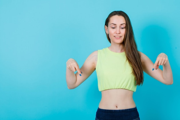 Regardant vers le bas, la fille pointe vers le bas avec les index sur fond bleu