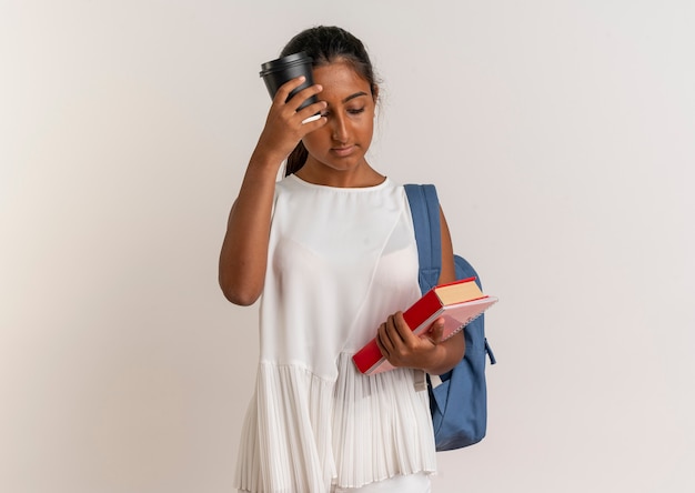Regardant vers le bas jeune écolière portant un sac à dos tenant un livre avec un ordinateur portable et une tasse de café sur le front