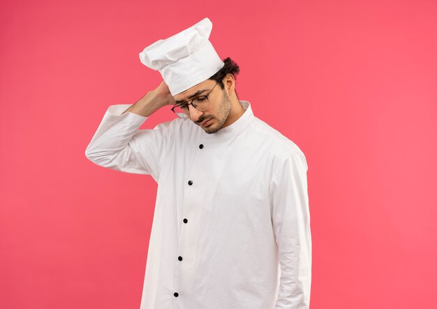 Regardant vers le bas jeune homme triste cuisinier portant l'uniforme de chef et des lunettes mettant la main sur la tête