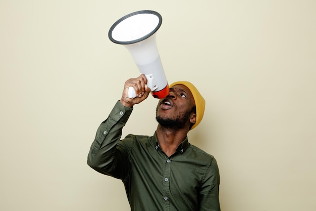 Regardant vers le haut un jeune homme afro-américain en chapeau portant une chemise verte parle sur un haut-parleur isolé sur fond blanc