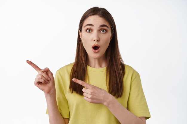 Regarde ça. Impressionné caucasian girl pointant vers la gauche debout sur blanc