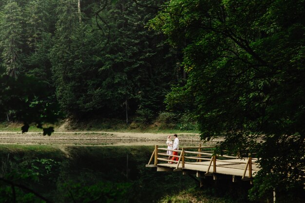 Regarde de loin chez un beau couple debout sur un porche en bois sur un lac de montagne