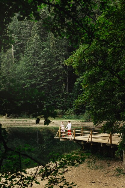 Regarde de loin chez un beau couple debout sur un porche en bois sur un lac de montagne