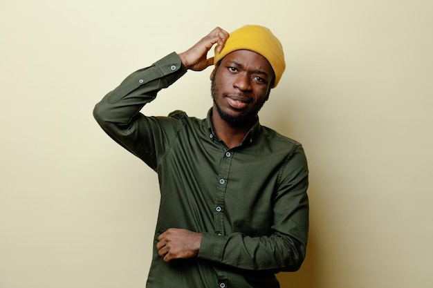 Regarder La Caméra En Mettant La Main Sur La Tête Jeune Homme Afro-américain Au Chapeau Portant Une Chemise Verte Isolée Sur Fond Blanc