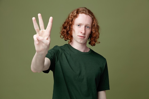 Regarder la caméra montrant trois jeunes beau mec portant un t-shirt vert isolé sur fond vert