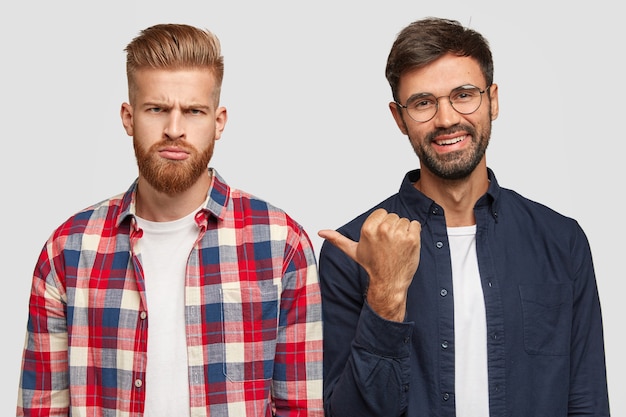 Photo gratuite regardez ce gars. un homme mal rasé souriant indique avec le pouce à un ami sombre qui n'est pas satisfait des résultats de l'examen