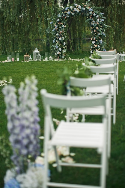 Regardez par derrière à des chaises blanches sur la pelouse verte avant l&#39;autel du mariage