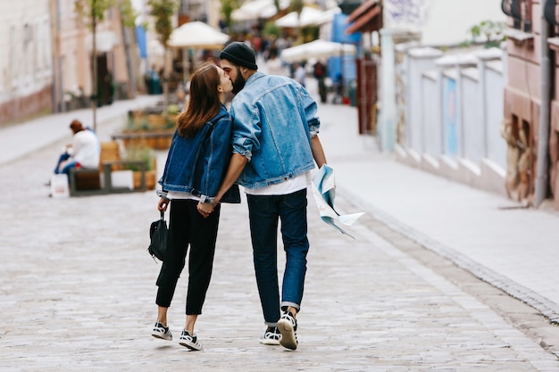 Regardez par derrière le couple de touristes tenant leurs mains ensemble en marchant autour de la ville