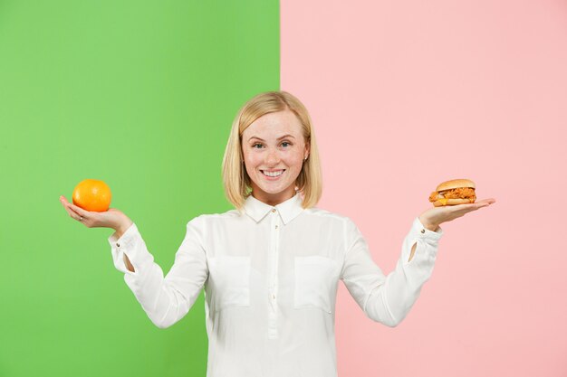 Régime. Concept de régime. La nourriture saine. Belle jeune femme choisissant entre les fruits et la restauration rapide sans hâte