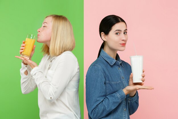 Régime. Concept de régime. La nourriture saine. Belles jeunes femmes choisissant entre le jus d'orange aux fruits et une boisson sucrée gazeuse sans hâte