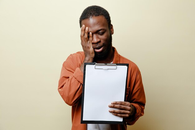 Regret visage couvert avec la main jeune homme afro-américain tenant le presse-papiers isolé sur fond blanc