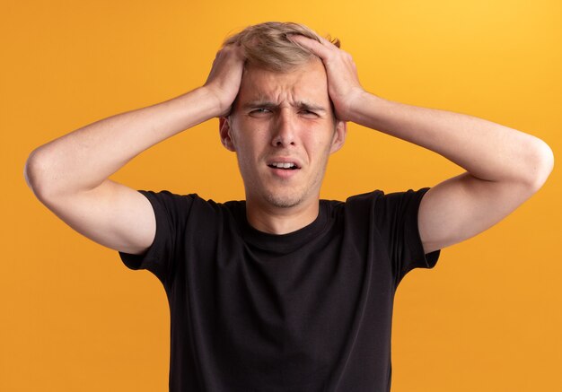 Regretté jeune beau mec portant une chemise noire a attrapé la tête isolée sur le mur jaune