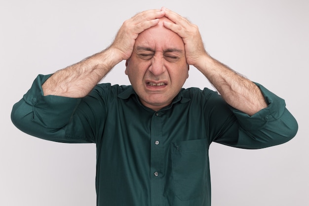 Regretté les yeux fermés homme d'âge moyen portant un t-shirt vert attrapé la tête isolé sur un mur blanc