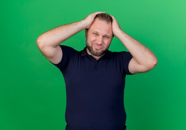 Regretter l'homme slave adulte mettant les mains sur la tête à la recherche d'isolement sur le mur vert