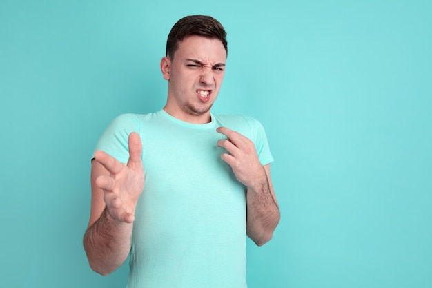 Rejetant, dégoûté. Portrait de jeune homme caucasien isolé sur mur bleu. Beau modèle masculin dans un style décontracté, couleurs pastel. Concept d'émotions humaines, expression faciale