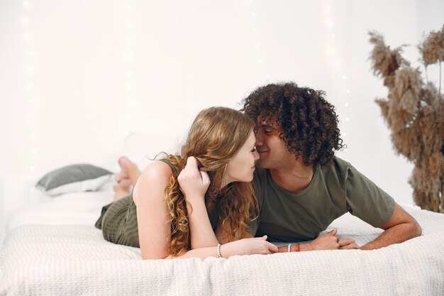 Relation amoureuse. Un couple joyeux s'amuse sur un lit. Chambre moderne blanche.