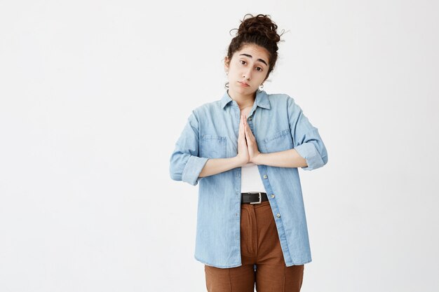 Religieuse jeune femme brune aux cheveux noirs se tenant la main dans la prière dans l'espoir de fortune. Religion, concept de spiritualité. Triste étudiante en chemise en jean mendiant pour la marque